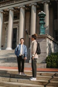 Full body of multiethnic friends having conversation on stone stairs of historic university with columns